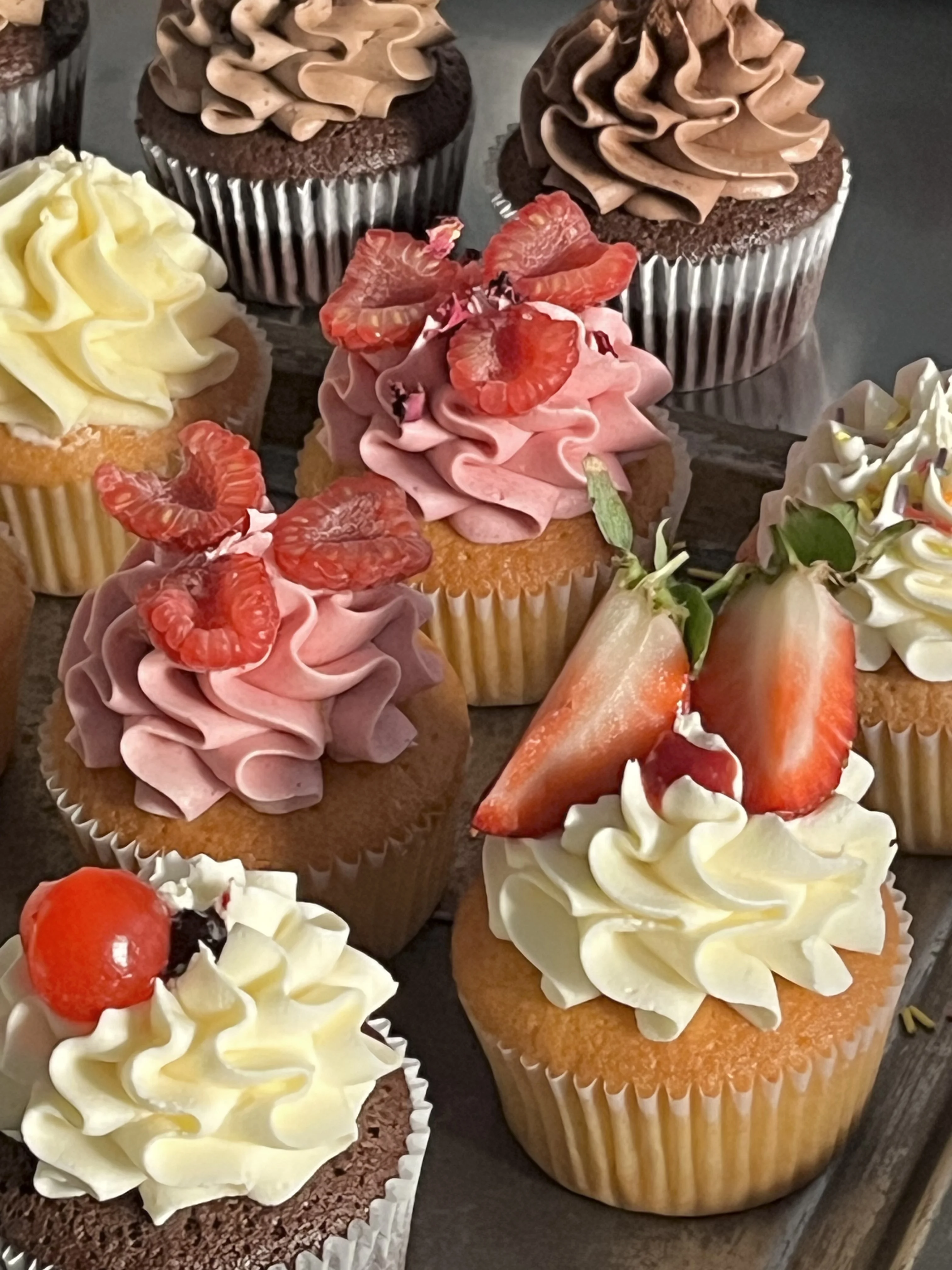 Assorted buttercream cupcakes topped with strawberries and raspberries