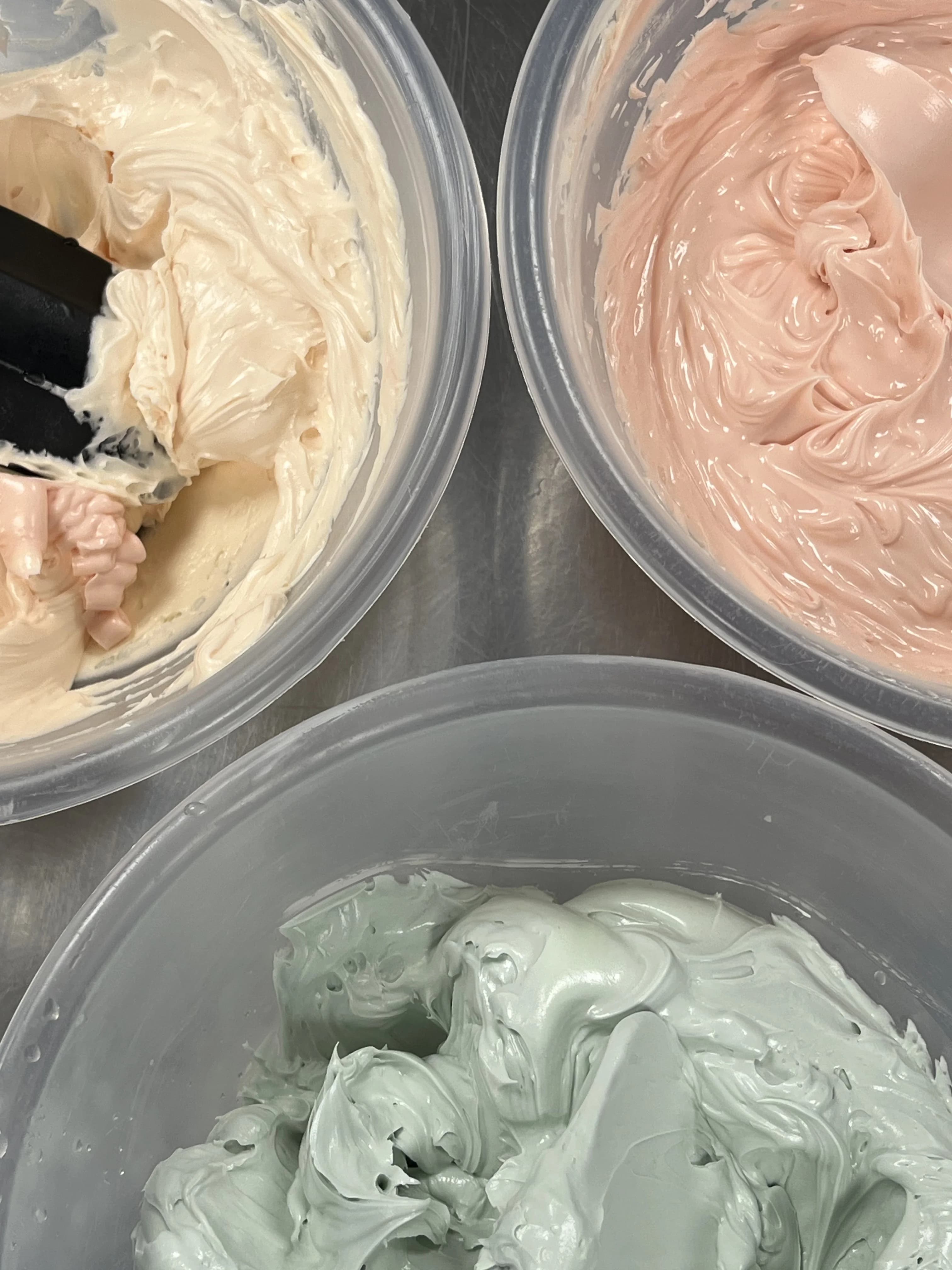 Bowls of cream, pink and sage buttercream ready for piping