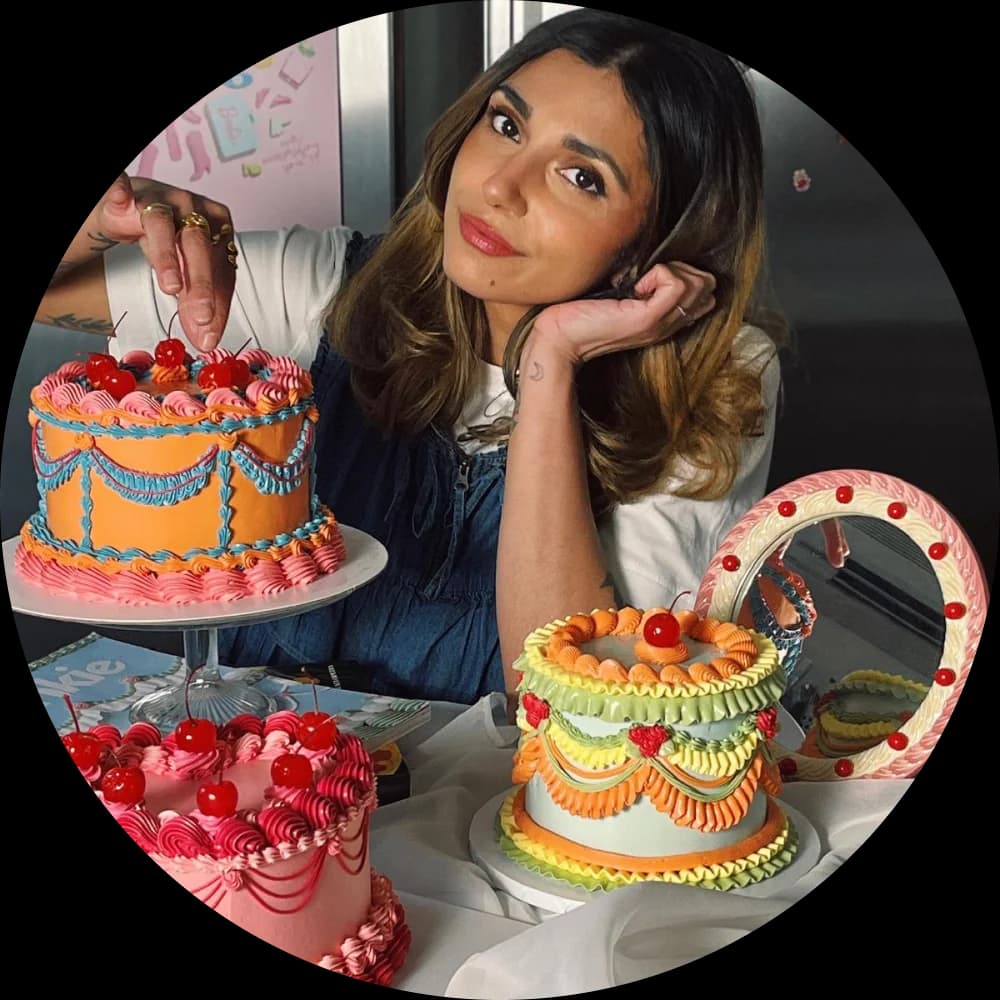 Roxy Mankoo leaning between two vintage-style buttercream cakes