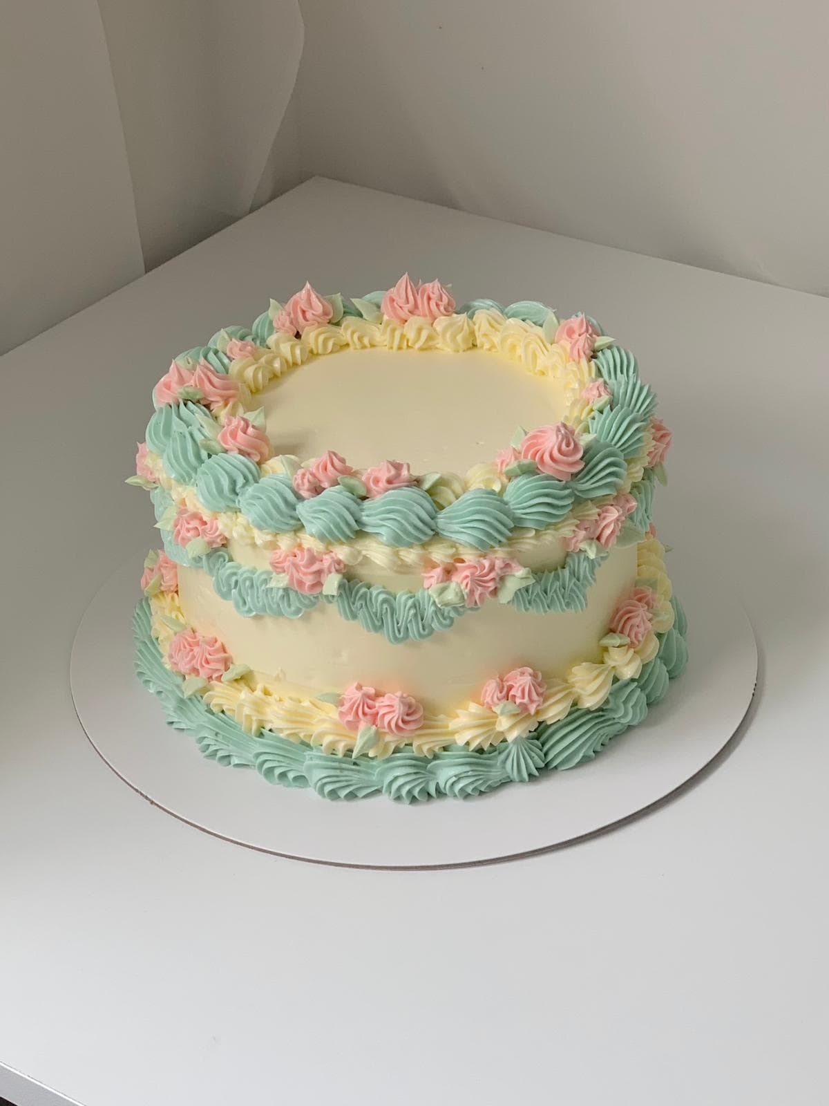 Cream vintage-style cake with teal and pink piped details made by a student