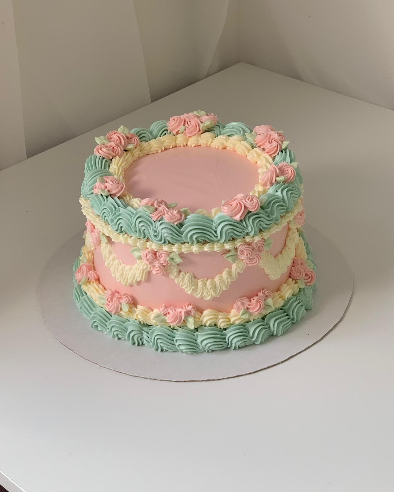 Pink vintage-style cake with teal shell borders and yellow piping made by a student
