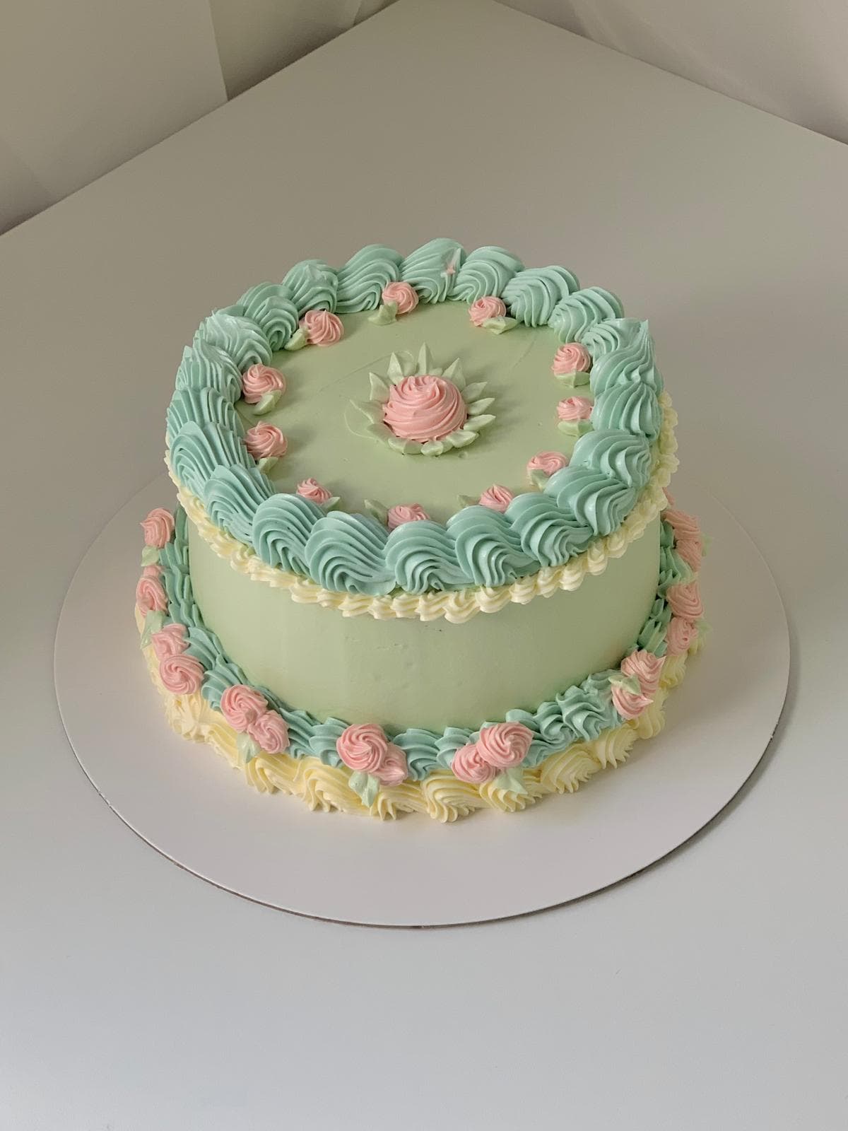 Green vintage-style cake decorated with teal swirls and pink rosettes made by a student